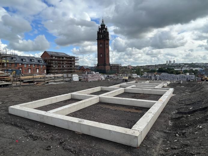 Concrete beams laid on the ground outside with a church tower in the background