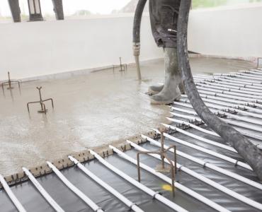 Concrete being poured inside a building over an underfloor heating system