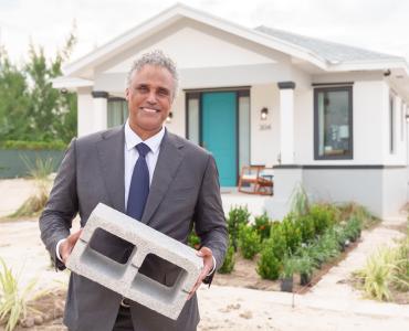 A man holding a concrete block outside a small house