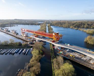 An aerial shot of a red bridge launcher crossing a river and canal