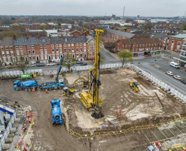 An aerial photo of a construction site with blue concrete mixers and concrete pump, and a yellow foundation rig