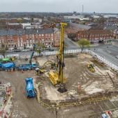 An aerial photo of a construction site with blue concrete mixers and concrete pump, and a yellow foundation rig