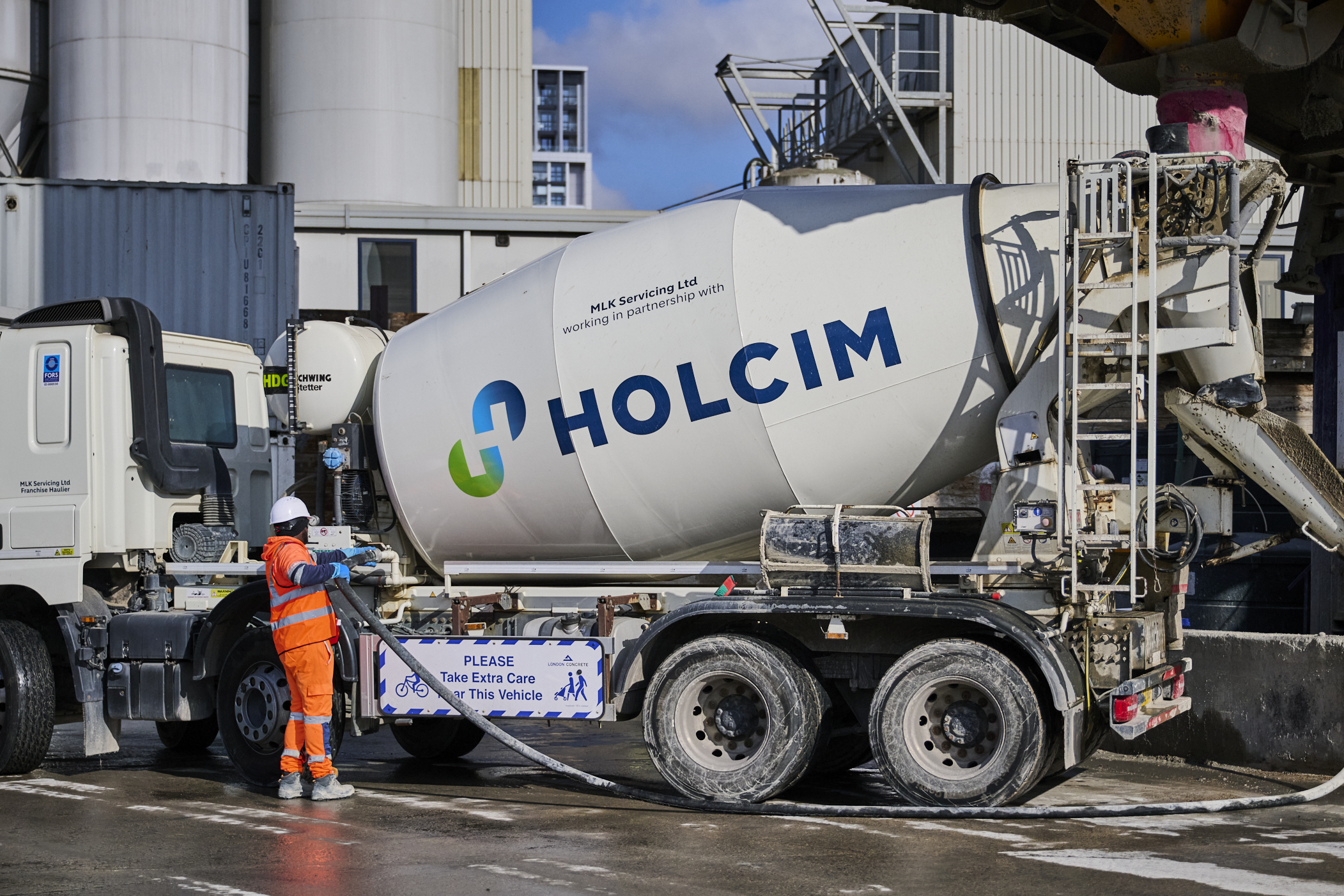 A Holcim branded cement truck with an operative standing next to it in orange PPE.