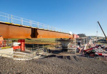 A steel bridge deck being slid into position with a crane in the background