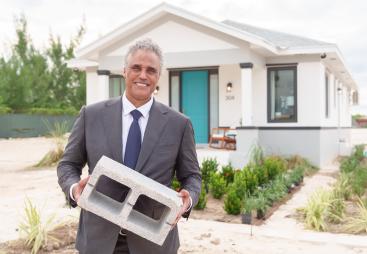 A man holding a concrete block outside a small house