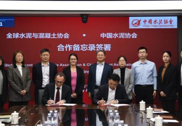 Several people standing around a table looking at two men signing a document