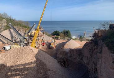 A picture of a yellow crane in a quarry with the sea in the background