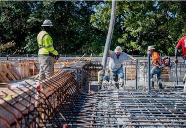 Four US construction workers in bright tshirts and PPE pour concrete