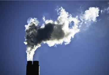 The top of a smoking industrial chimney with black and white smoke billowing from the top