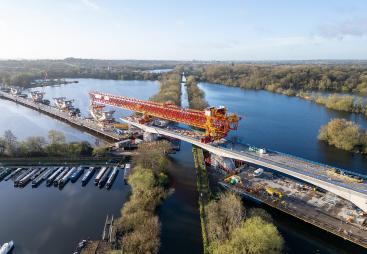 An aerial shot of a red bridge launcher crossing a river and canal