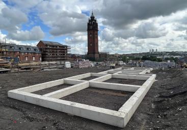 Concrete beams laid on the ground outside with a church tower in the background