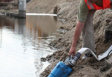 A man in red PPE holds a dewatering pump in water
