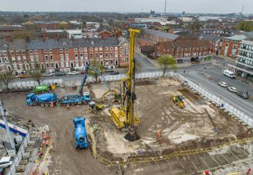 An aerial photo of a construction site with blue concrete mixers and concrete pump, and a yellow foundation rig