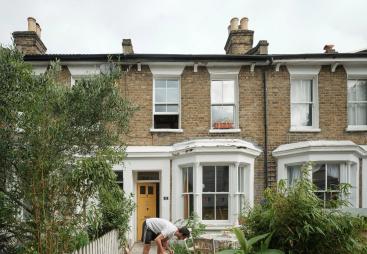 A man in shorts working in the front garden of a victorian terrace house