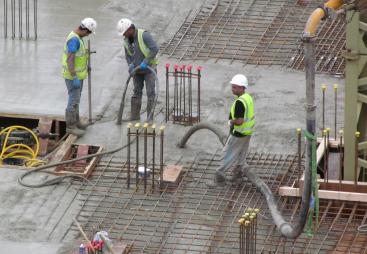 Three UK construction workers in PPE using a concrete pump to place concrete