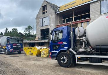 Two blue and grey concrete mixer trucks outside a new build house