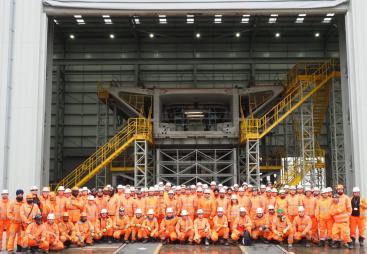 A group of people orange PPE standing in front of a precast concrete bridge pier