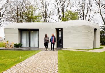 Two people walking down the garden path from a single story house