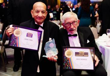 Two old men in DJs holding award certificates