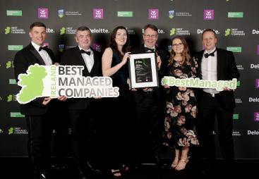 A group of men and women in evening wear at an awards ceremony holding a map of Ireland, a certificate and some cut-out words