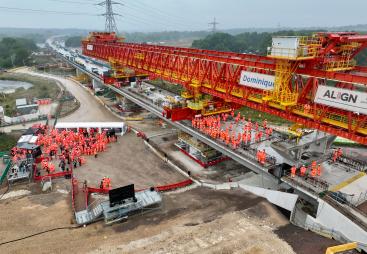 Two large groups of people in orange PPE standing on an under construction bridge deck