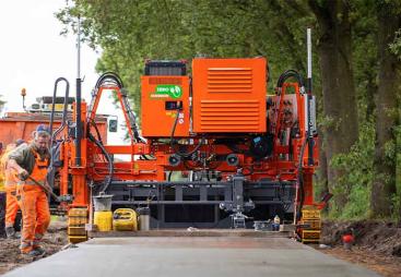 Men in orange PPE working on a raod paving project with an electric slipform paver