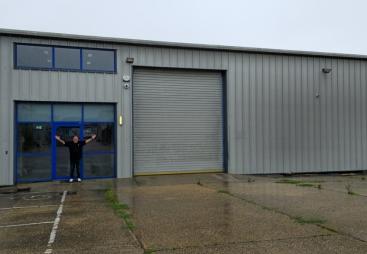 A bald man dressed in black outside a non-descript industrial estate