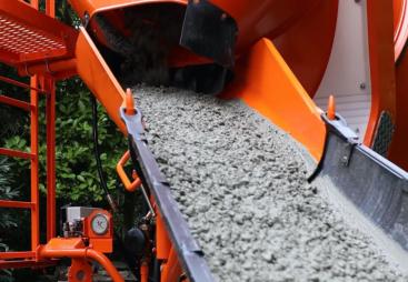 A close up of an orange cement mixer's chute discharging concrete