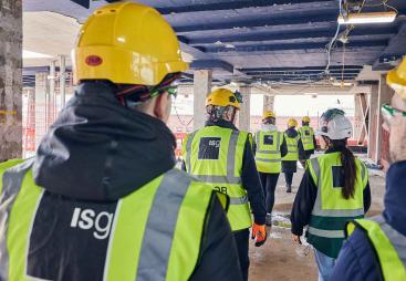 A group of people in PPE walking away from the viewer inside an under construction office building