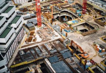 A costruction site with several peices of equipment including a red tower crane and a yellow excavator
