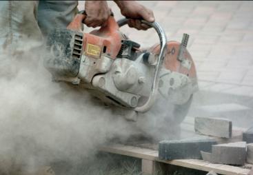 A close up of a hand-held concrete saw in use with silica dust clouds