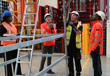 Three men in orange PPE and one in yellow inspect scaffolding