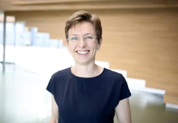 A head and shoulders photo of a woman with short hair, glasses and wearing a black tshirt
