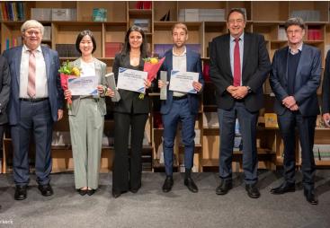 A line of people, some of whom are holding certificates,  standing in front of shelves celebrate winning the 2024 Förderpreis Beton Central Europe Competition