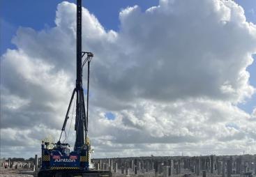 A Junttan piling rig stands in front of hundreds of pile caps, with a blue sky and dramatic clouds
