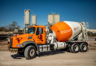 A bright orange concrete mixer truck at a cement plant