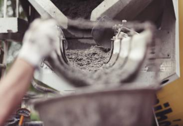 Concrete being poured from a mixer into a container. A dynamic action image shows wet concrete being dispensed from a mixer into a container, capturing the essence of construction work and the creation of solid foundations in building projects.