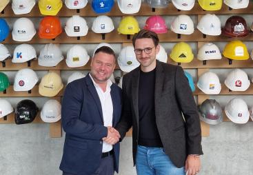 Christoph Miks (director customer solutions, core sensing), Michel Seeger (CEO, Vemaventuri) shake hands in front of a wall of multi-coloured construction hats