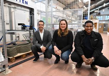 Three people crouch in front of the UK's first 3-D concrete printer
