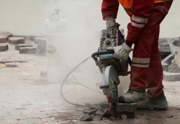 A man in red PPE using a hand-held concrete saw to repair a pavement