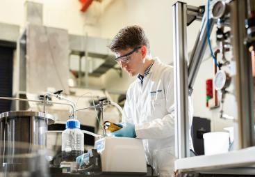 A man in lab coat and safety goggles working in a laboratory.