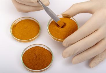 A close up of two hands holding one of three vials with a variety of orange powder