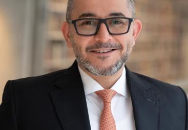 Mohamad Al-Dah, the new IStructE President 2025, in a dark suit, white shirt, glasses and an orange tie.