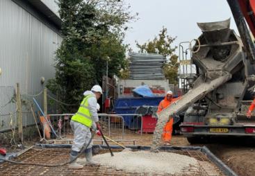 Workers at a construction site spread concrete being discharged by a mobile concrete mixer