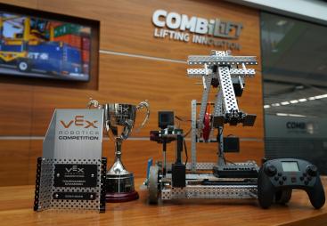 The Vex Robotics Awards on a table in front of a Combilift sign and video display showing a yellow and blue robotic vehicle