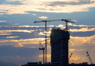A High rise building under construction in silhouette with the sun setting behind it with three tower cranes