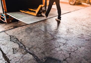 A man using a yellow trolly to unload a lorry onto a loading dock