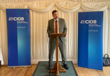 Mike Reader MP, the new chair of the All-Party Parliamentary Group for Excellence in the Built Environment, stands behind a podium, flanked by CIOB banners, speaking at the launch of the CIOB's Construction Client Guide: Leading Projects in the Built Environment, in Parliament last week.