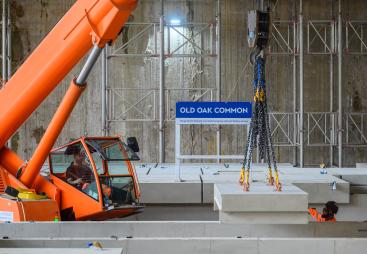 An orange crane and orange PPE-clad worker installing the first platforms at HS2's Old Oak Common station for HS2 trains.