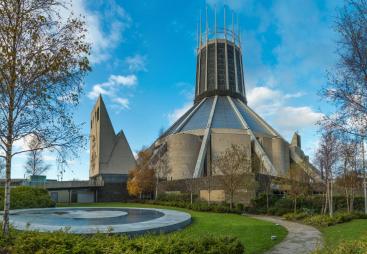 A view of Liverpool Metropolitan Cathedral in early summer with trees and a pond
